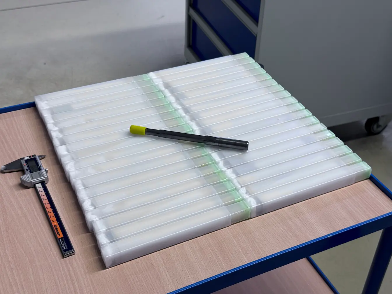 Weiße Kunststoff-Lithium-Ionen-Batteriezellen auf Tisch mit Schieblehre und Stift.