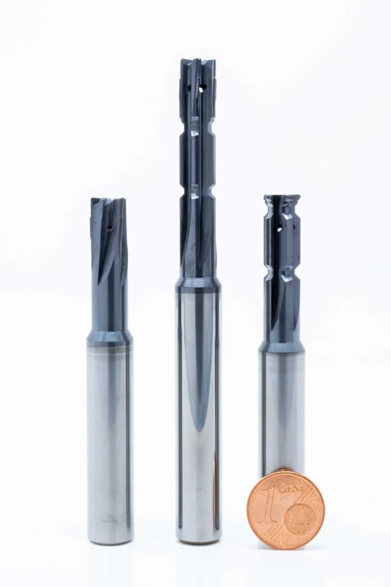 Drei metallische Fräswerkzeuge neben einem 1-Cent-Eurostück, angeordnet auf weißem Hintergrund.